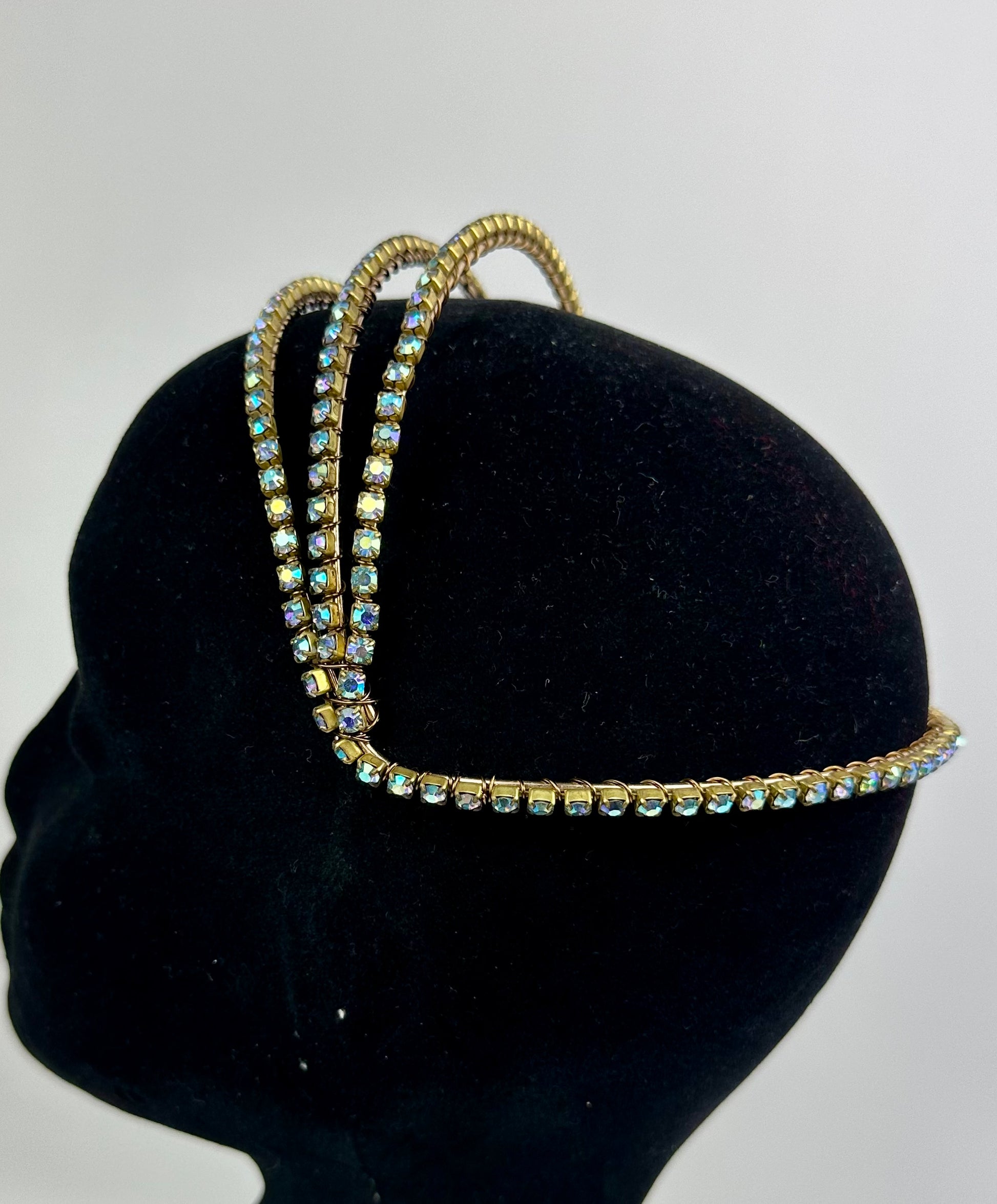 Three gold headbands with gemstones on a black mannequin head against a gray background