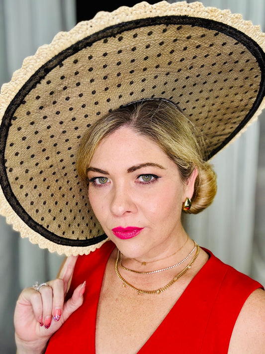 Woman wearing a large straw hat with a black dot pattern, posing against a neutral background.