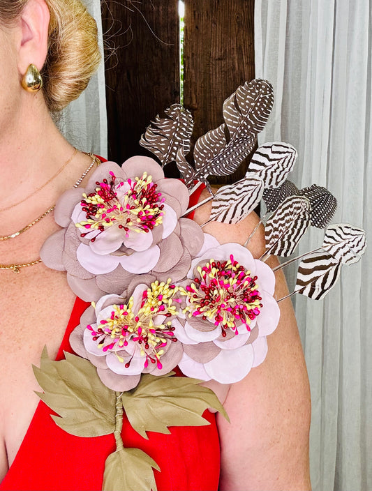 Person wearing a decorative dusty rose and pastel pink floral and feather accessory brooch with maroon, pink and yellow details against a neutral background