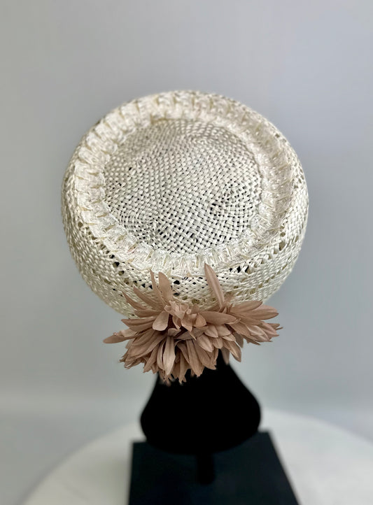 Cream-coloured woven pillbox hat with dusty rose beige floral design on back, on a black mannequin head against a gray background