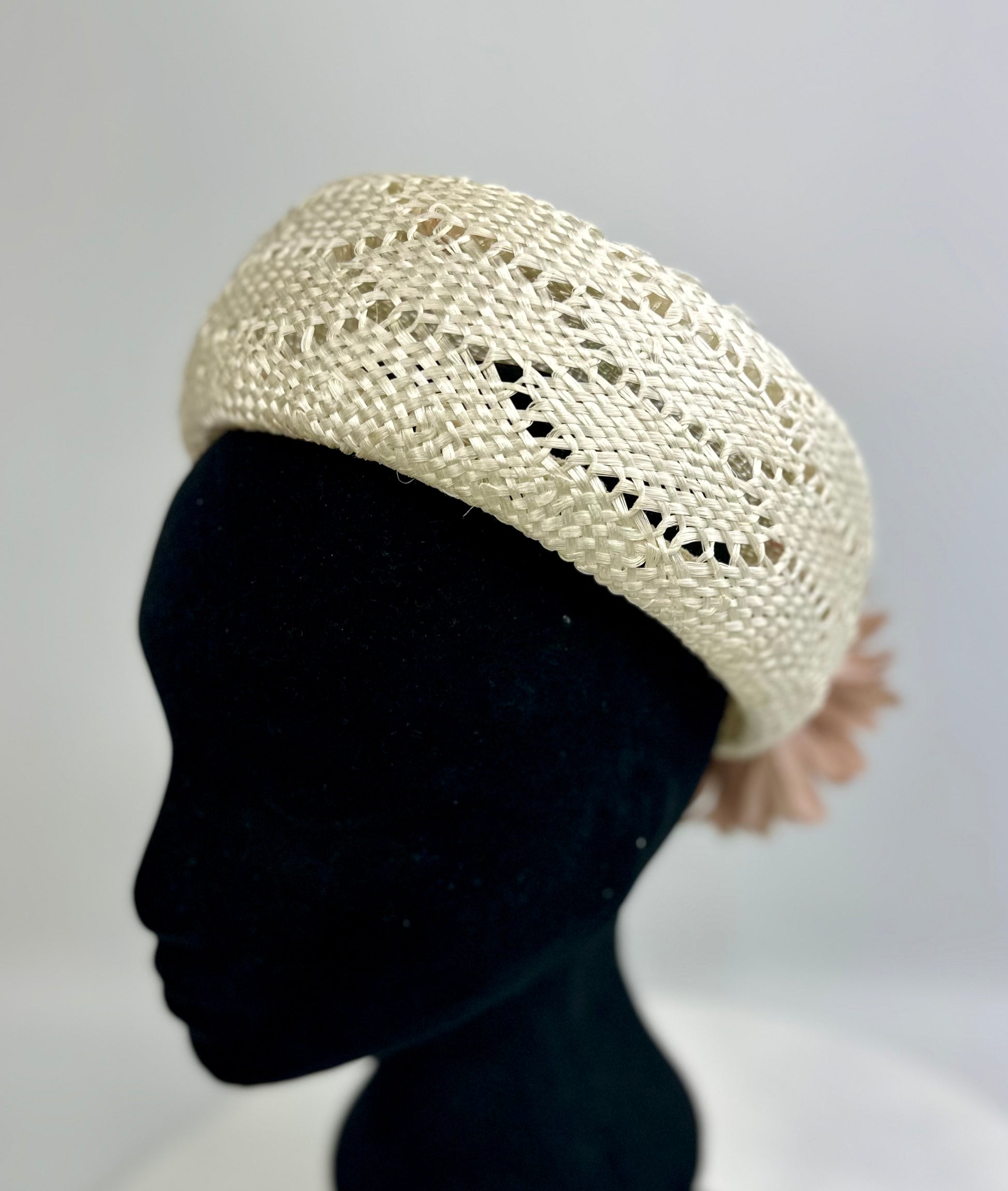 Cream-coloured woven pillbox hat on a black mannequin head against a gray background