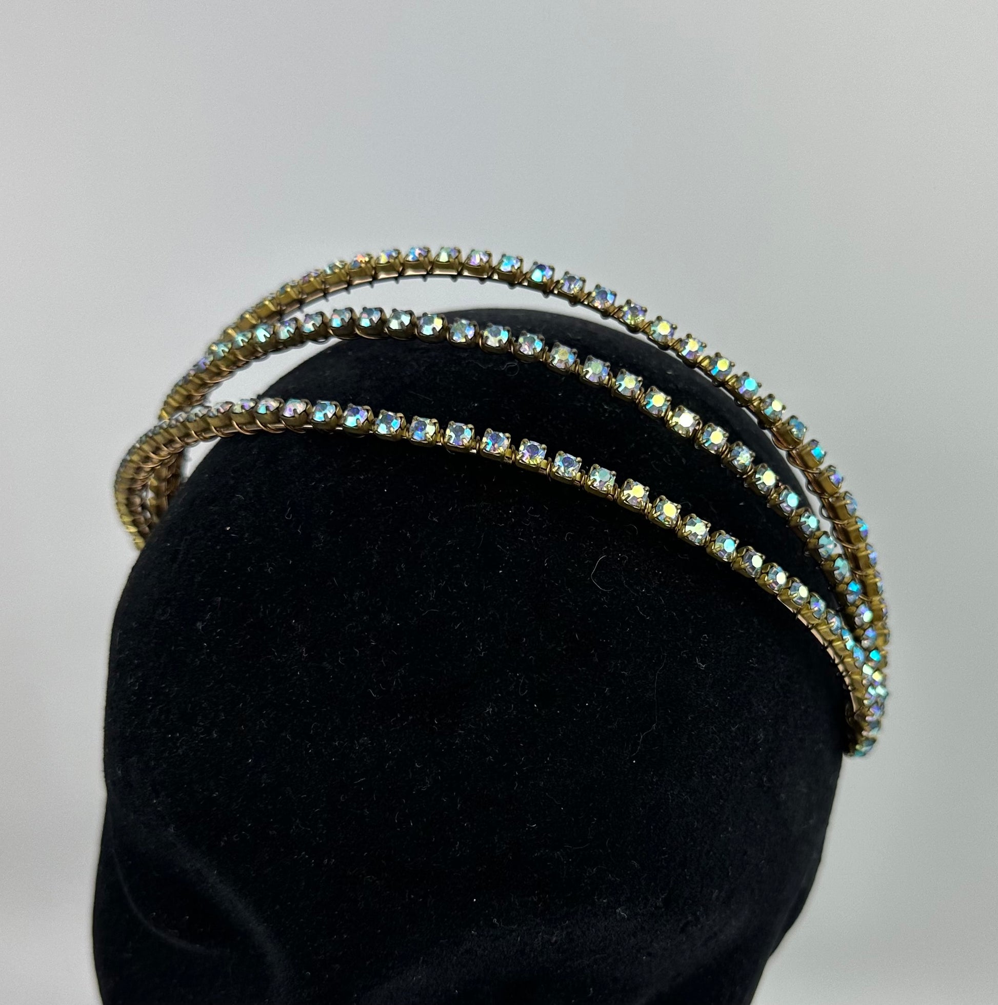 Three gold headbands with gemstones on a black mannequin head against a gray background
