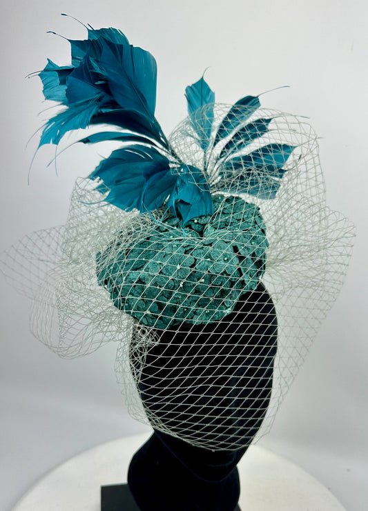 Abstract headpiece with teal box hat, blue teal feathers, white silver netting veil on white background