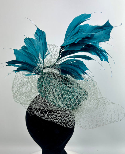 Abstract headpiece with teal box hat, blue teal feathers, white silver netting veil on white background