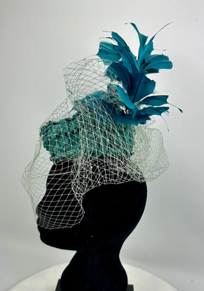 Abstract headpiece with teal box hat, blue teal feathers, white silver netting veil on white background