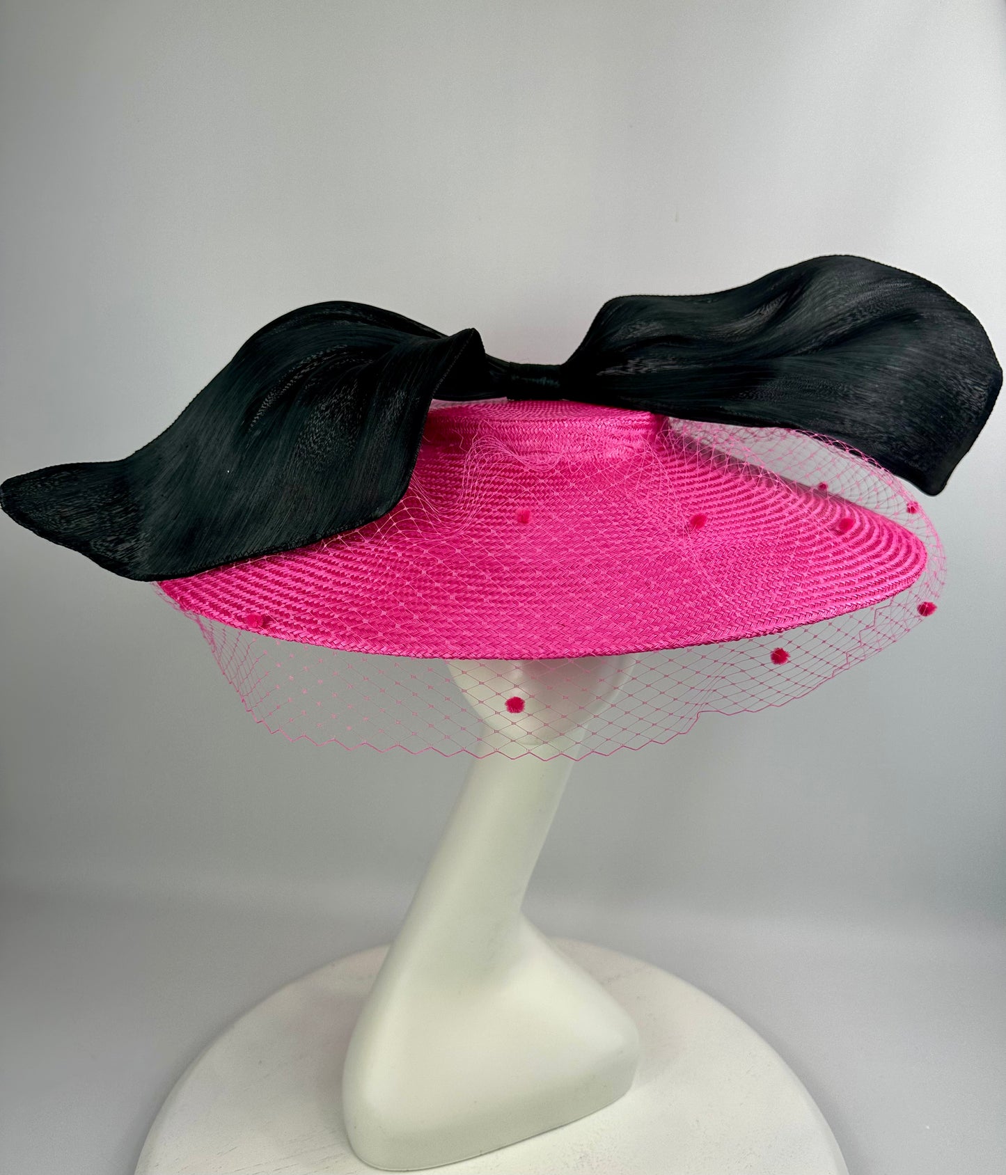 Pink hat with black bow on a white stand against a gray background