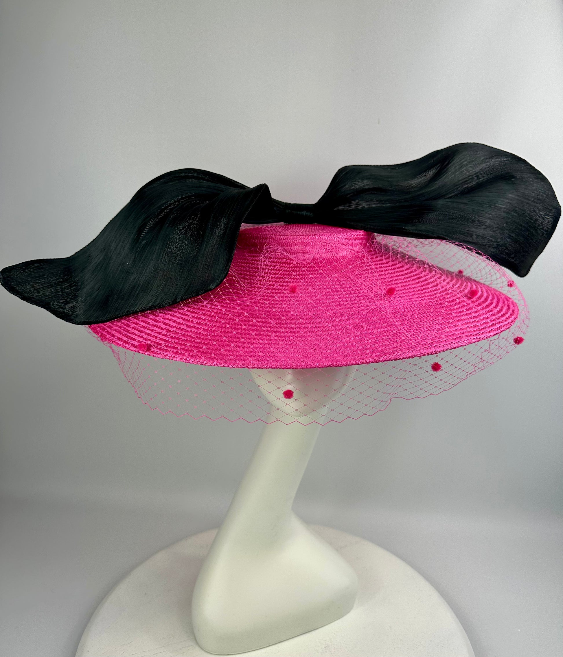 Pink hat with black bow on a white stand against a gray background