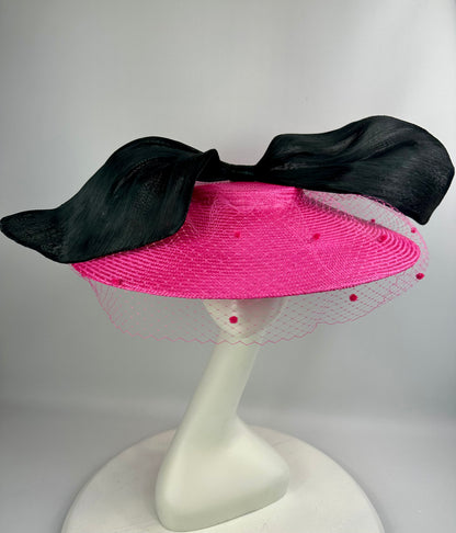 Pink hat with black bow on a white stand against a gray background