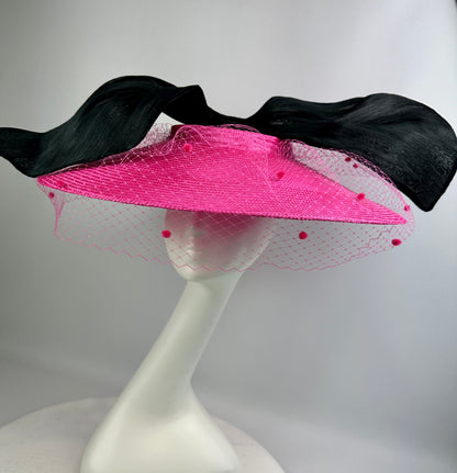 Pink hat with veil and black bow on a white stand against a gray background