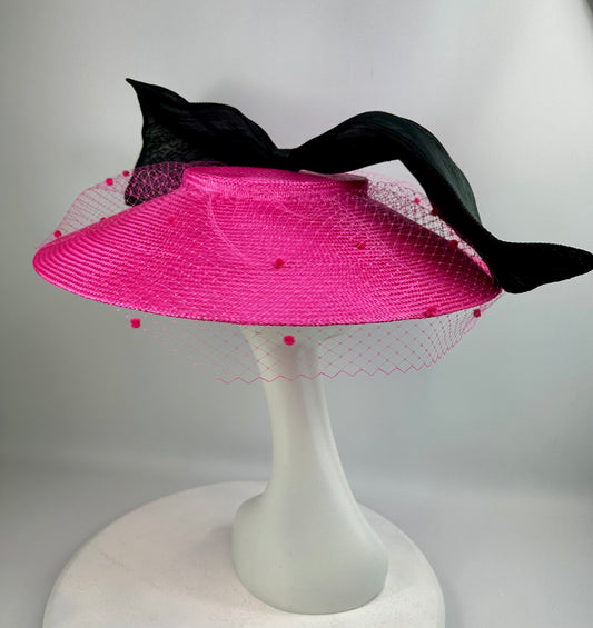 Pink hat with veil and black bow on a white pedestal against a light gray background