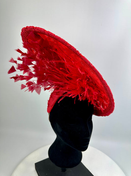 Red decorative hat with feather details on a black mannequin head against a white background
