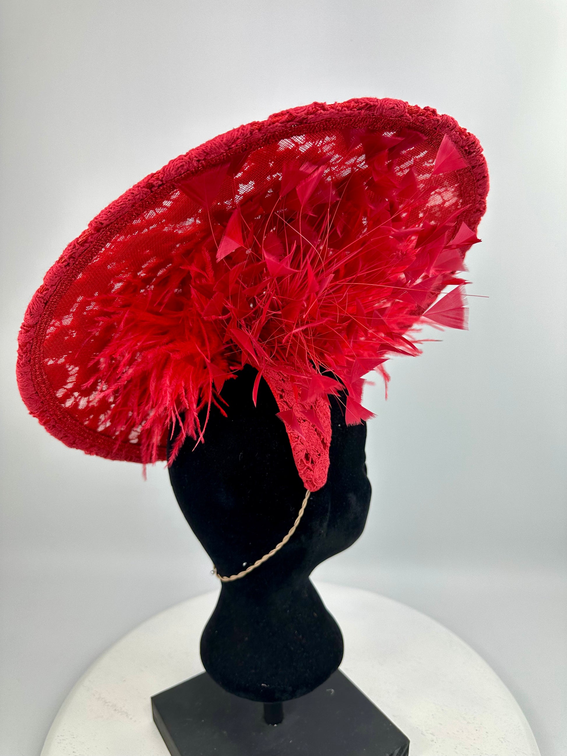 Red lace hat with feather details on a mannequin head against a white background