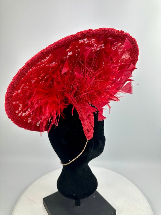 Red lace hat with feather details on a mannequin head against a white background