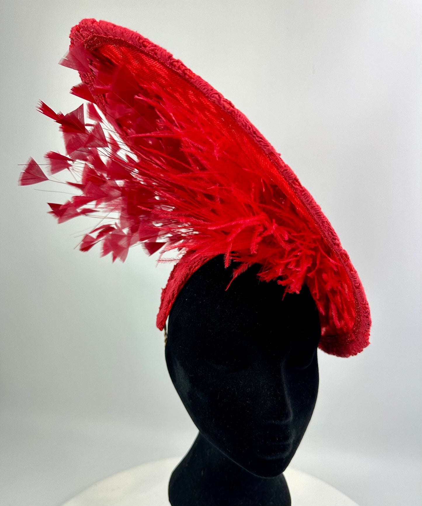Red feathered hat on a mannequin head against a white background