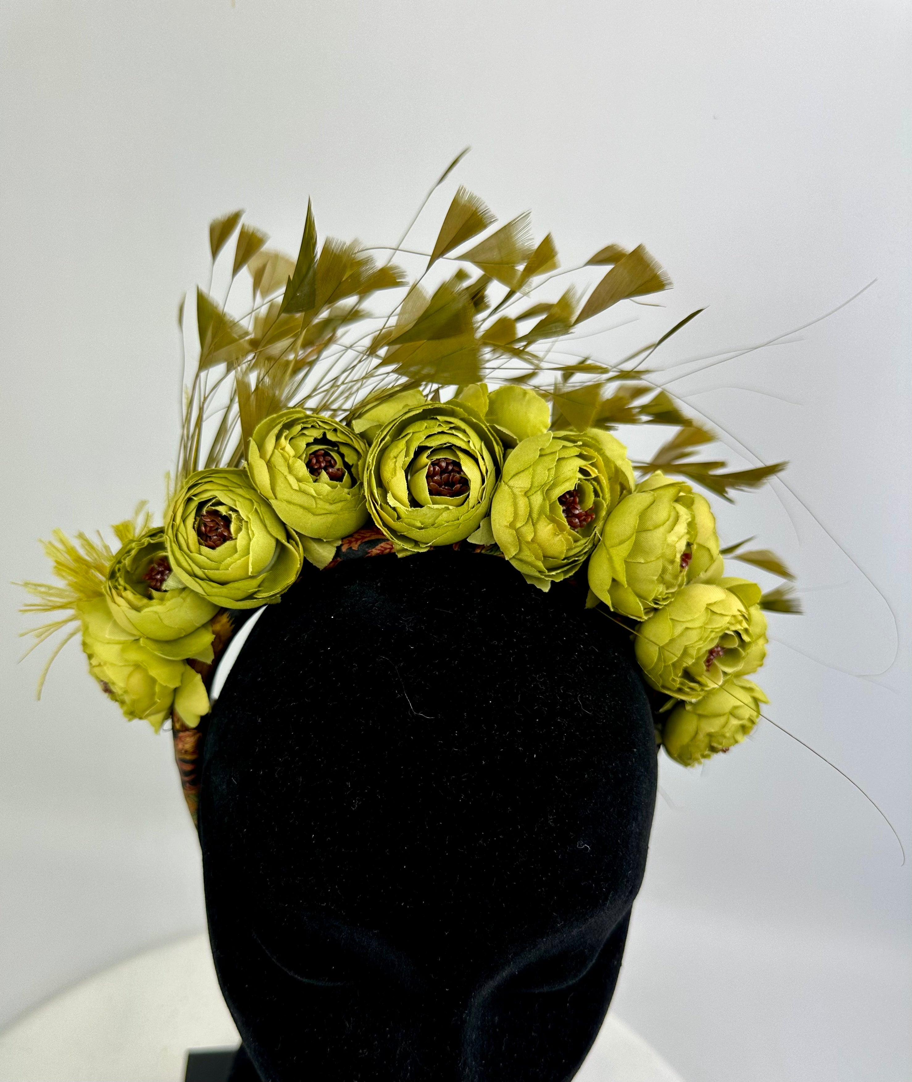 Floral headband with yellow green flowers on a black headform against a white background