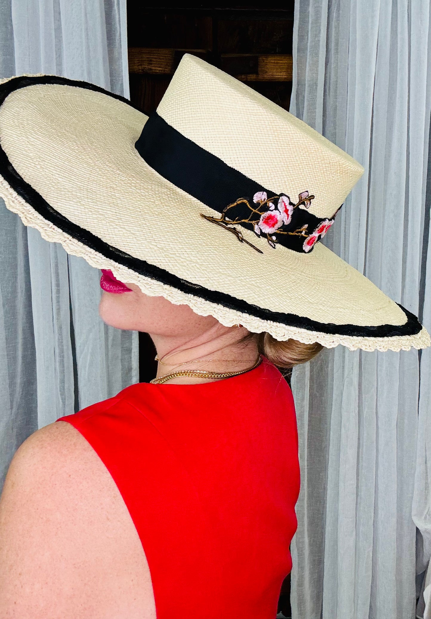 Woman wearing a wide-brimmed hat with floral details and a black band, against a neutral background.