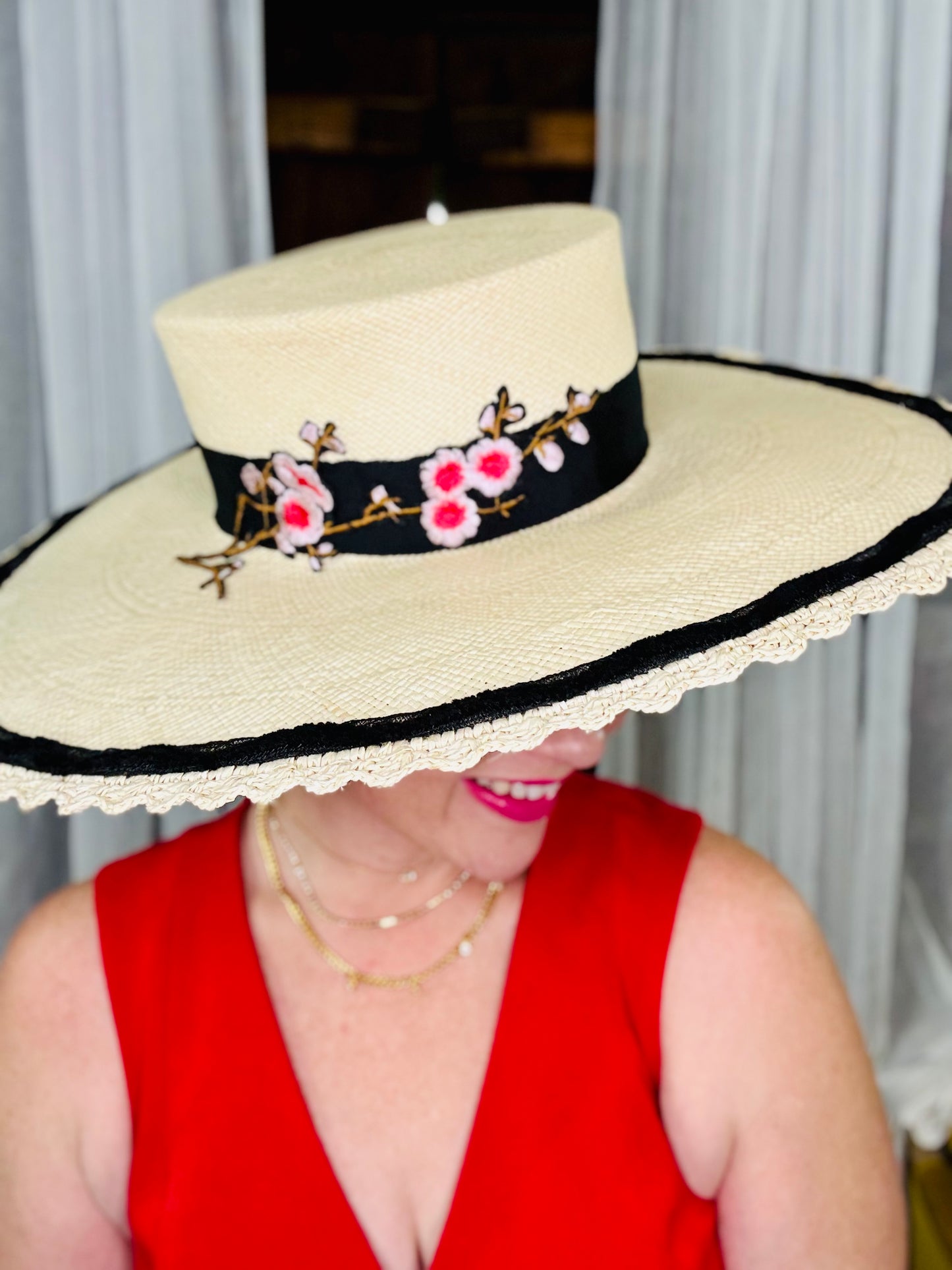Person wearing a wide-brimmed hat with floral embellishments and a red top.