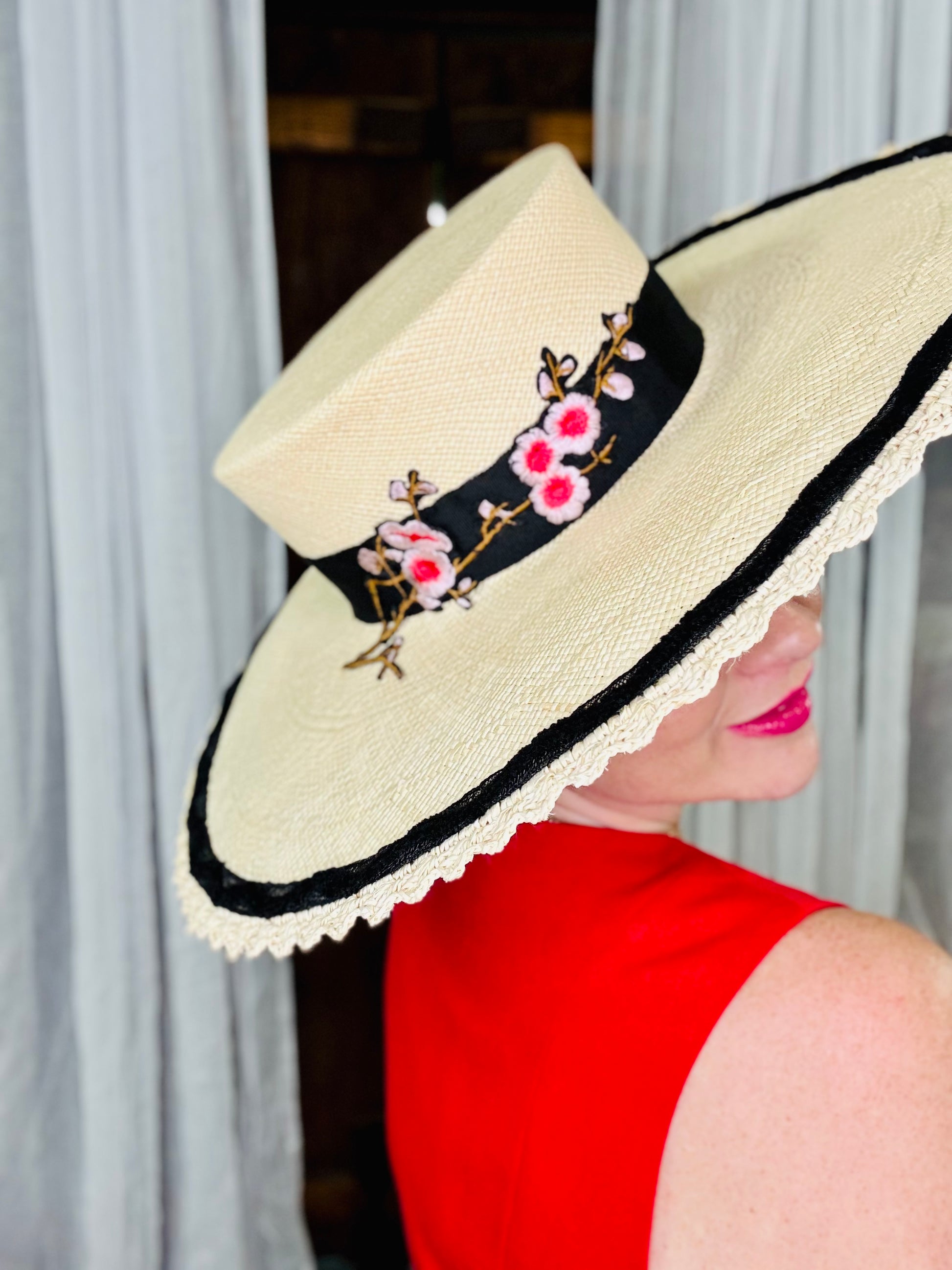 Woman wearing a decorative hat with floral embroidery against a neutral background