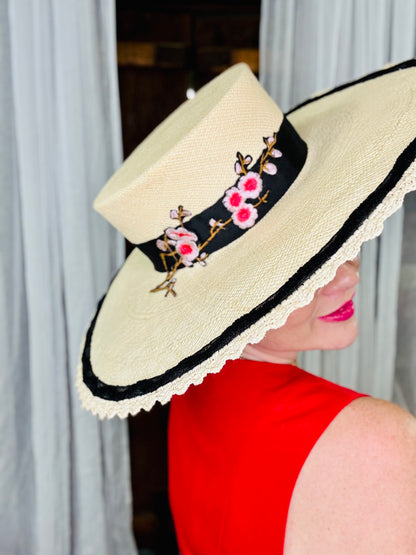 Woman wearing a decorative hat with floral embroidery against a neutral background