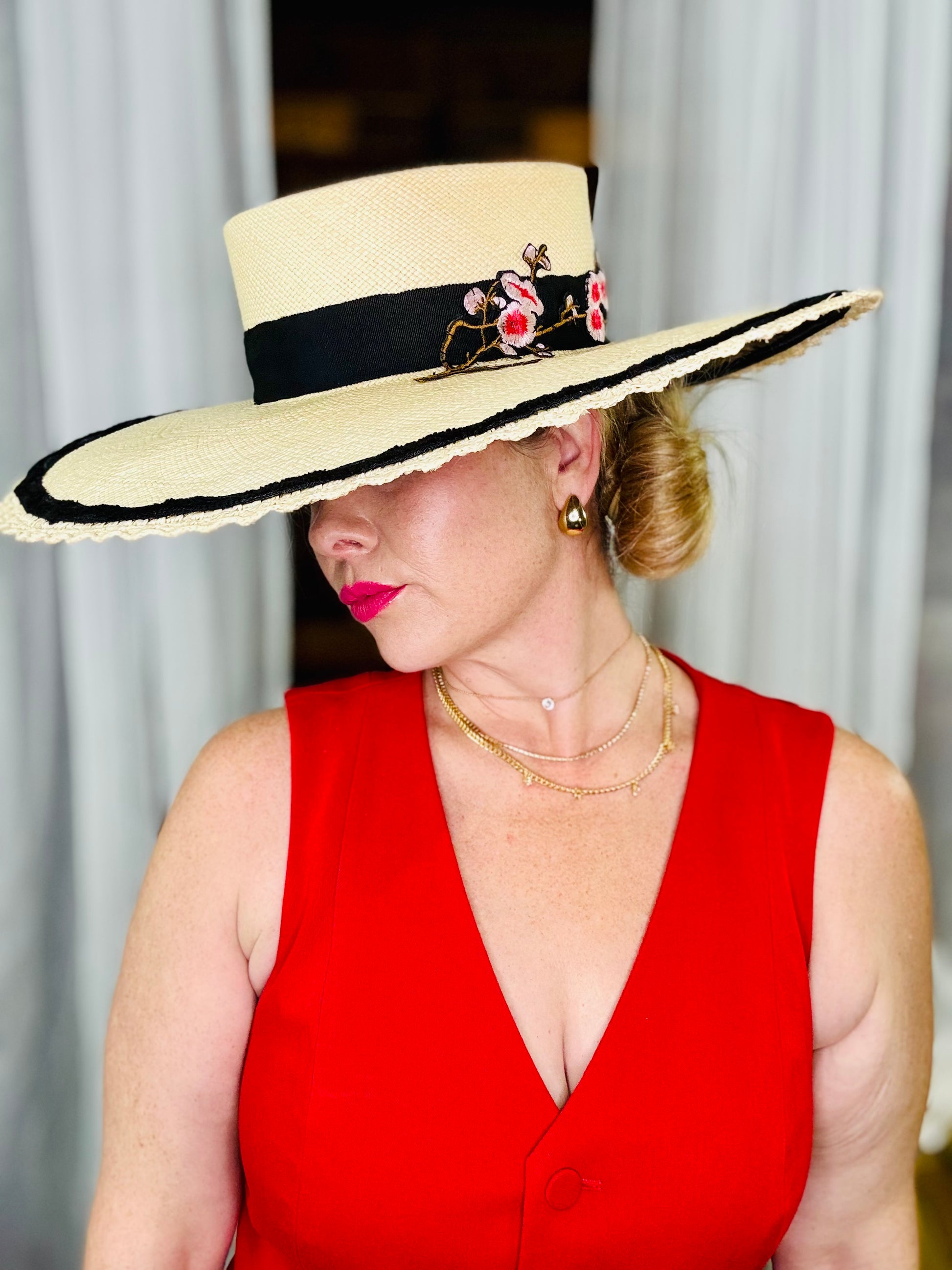 Woman wearing a wide-brimmed hat with floral details and a red dress.